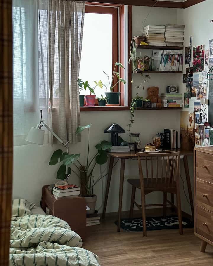 Natural-toned bedroom and home office corner featuring wooden desk, chair, curtains, and bookshelf with cozy atmosphere
