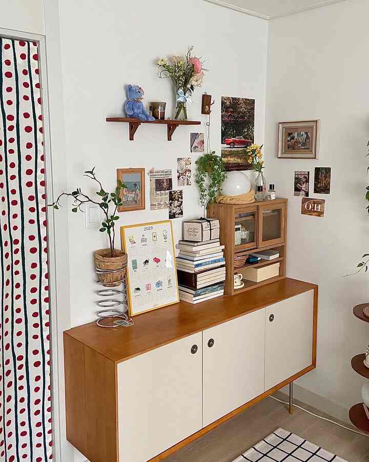 A cozy space with white walls and wood tone storage cabinet, featuring shelves, picture frames, posters, and plants blending harmoniously