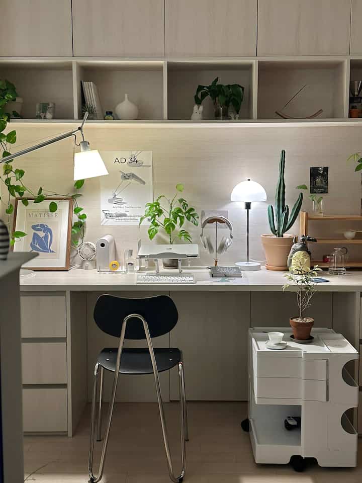 Natural wood-toned studio home office featuring white desk, black office chair, and dual lighting creating a cozy workspace