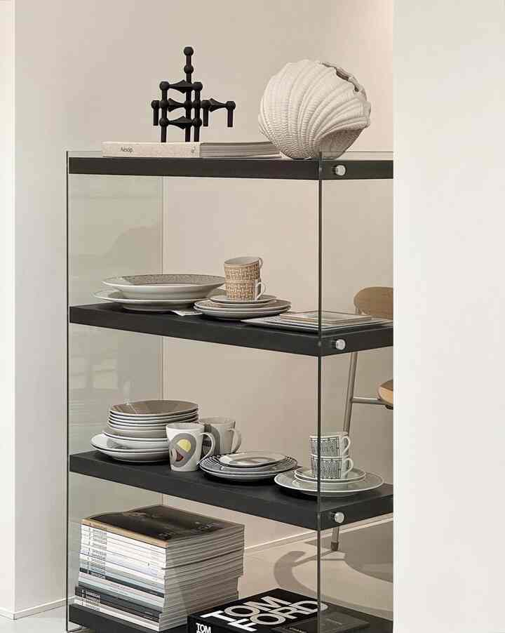 Mid-century modern living room in white and black tones featuring glass shelves with neatly arranged mugs and plates