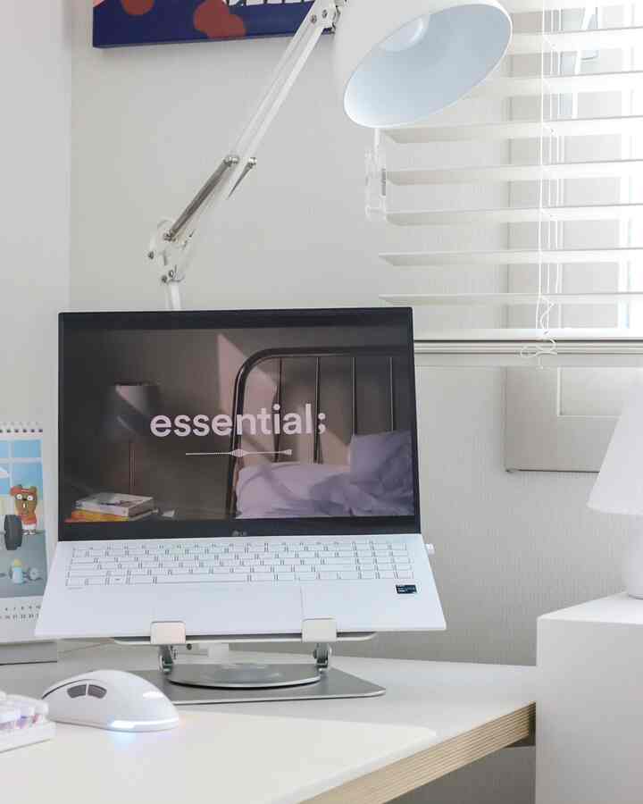 White-toned home office featuring LG Gram laptop on a monitor stand and task lighting with a simple, clean aesthetic