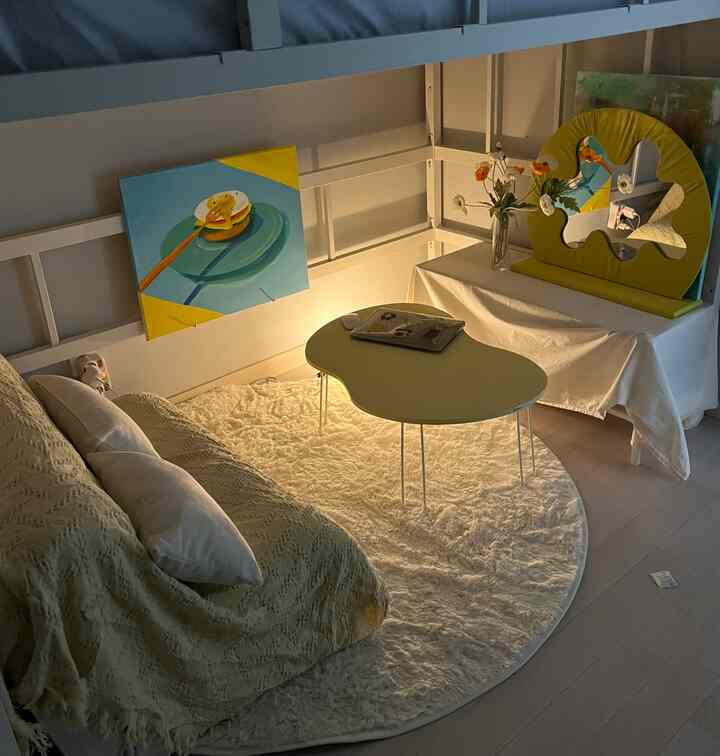White and yellow toned small low-ceiling bunker living room featuring rug, bed, table, and artwork with a cozy atmosphere