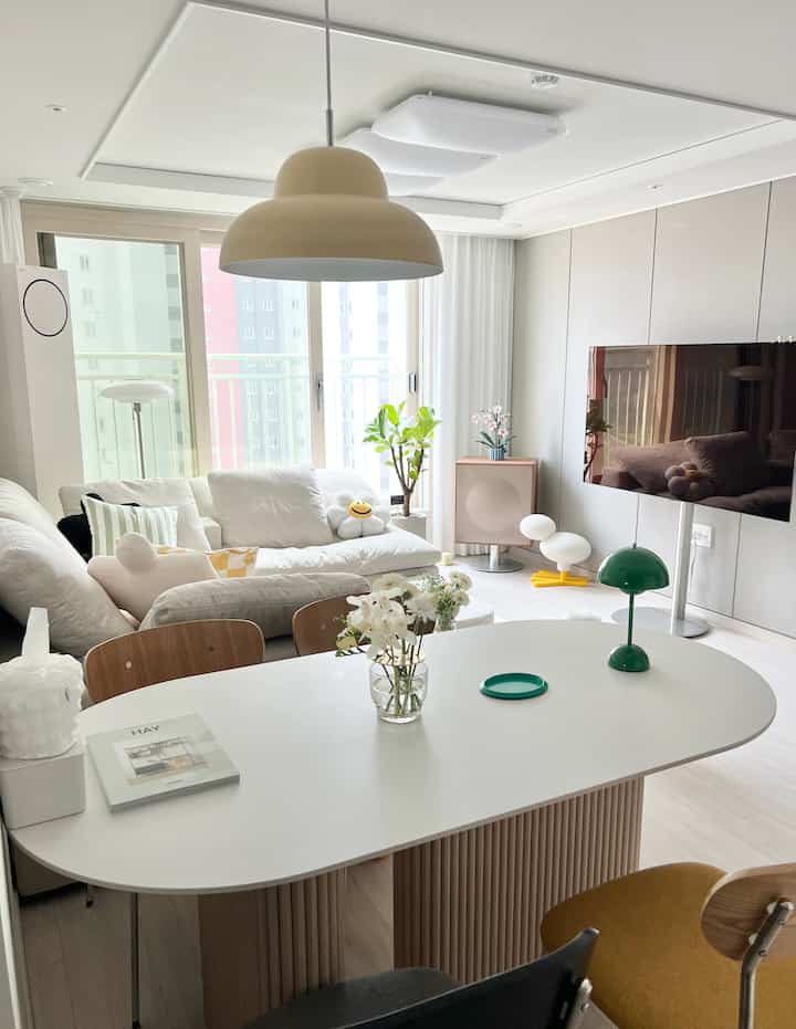 Bright living and dining room with white and natural wood tones, featuring a sofa, dining table, and green plant with a simple atmosphere