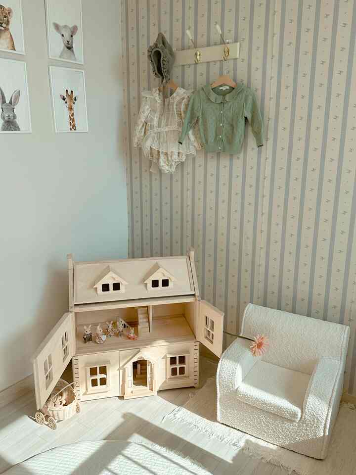Natural toned kids' room featuring a wooden dollhouse and a small white armchair with a cozy atmosphere