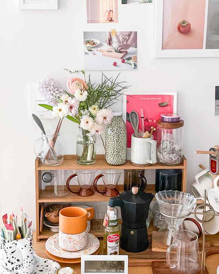 White-walled space featuring wooden shelving with coffee accessories and vases with flowers, creating a cozy home cafe atmosphere