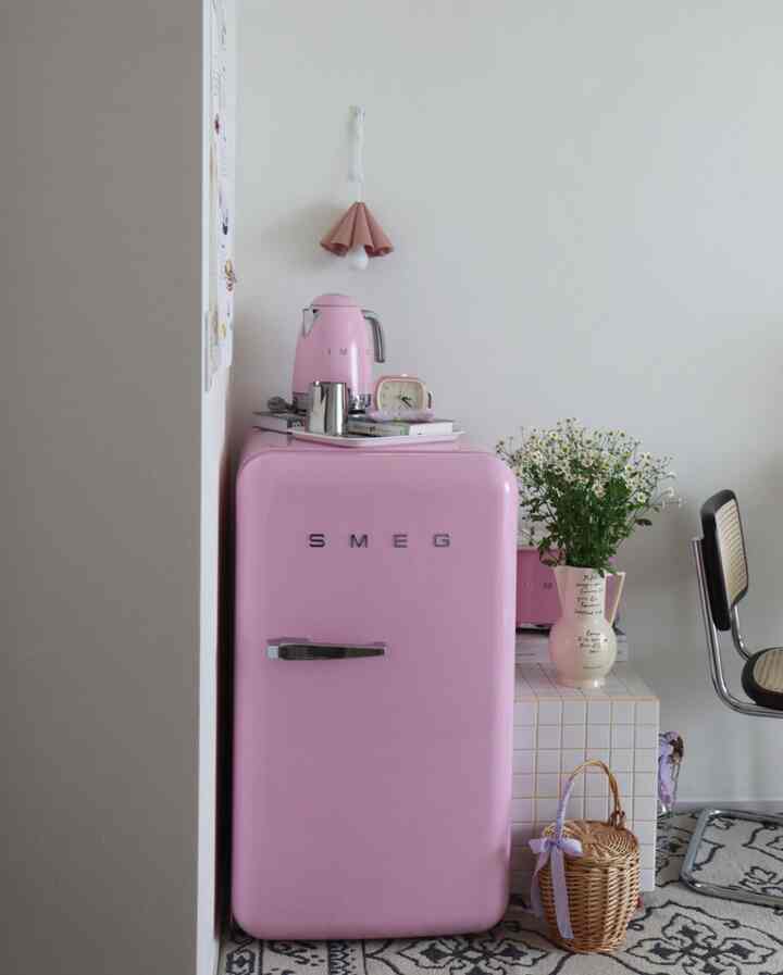 ピンクのスメグ冷蔵庫と電気ケトルがある白を基調としたキッチン、ナチュラルな小物とレトロな雰囲気が調和する空間