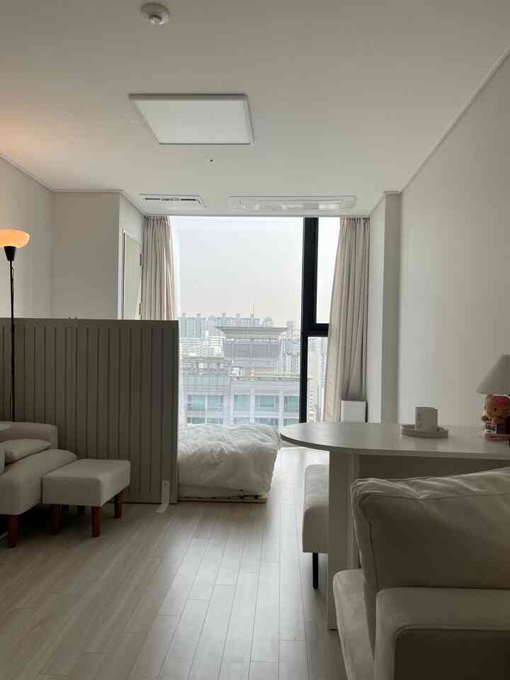 Warm ivory-toned studio apartment featuring a bed, sofa, and round dining table with a hotel-like interior atmosphere