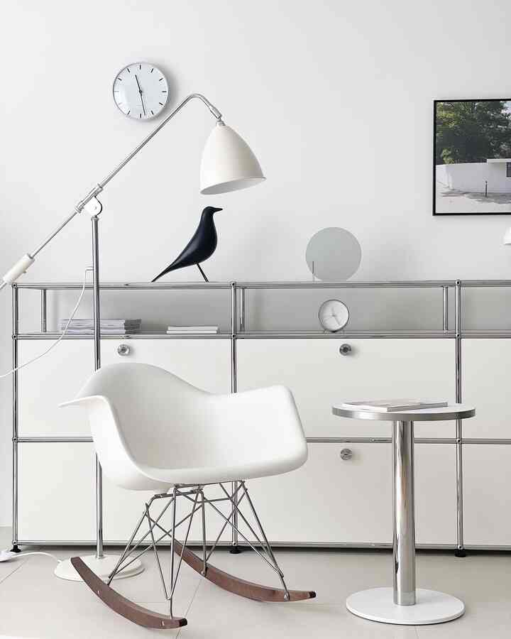 Modern living room in white and chrome tones featuring a white armchair, floor lamp, and clocks arranged neatly
