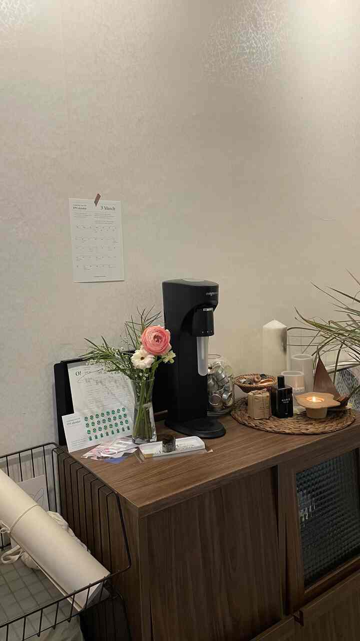 木目調の収納棚の上に炭酸水メーカー、花瓶、キャンドル、トレイが配置された温かみのある雰囲気の空間