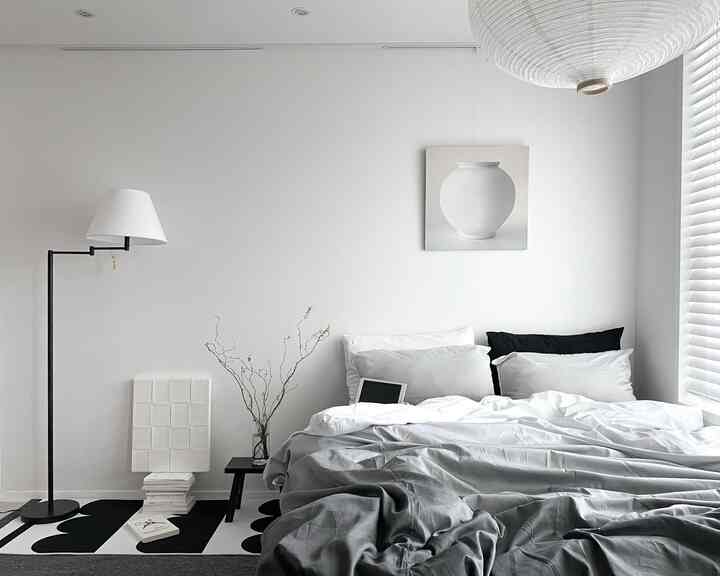 白と黒の寝室、シンプルでモダンな寝具とフロアランプが配置された清潔感のある空間