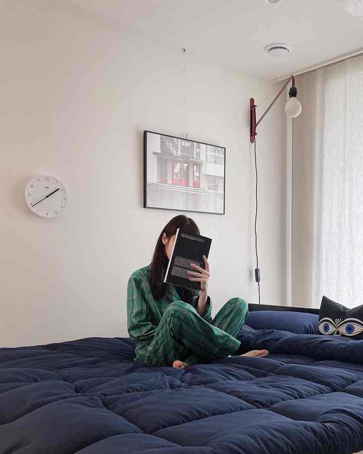 ネイビーの寝具と白い壁のシンプルな寝室、本を読む人がベッドに座っている印象的な空間