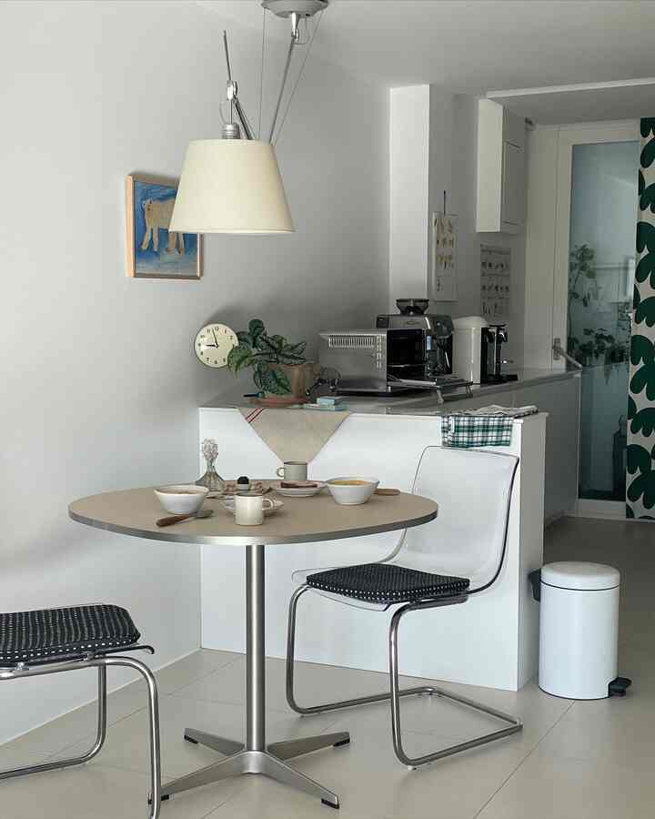 White-toned small kitchen and home cafe space featuring transparent chairs and round table with a simple, modern atmosphere