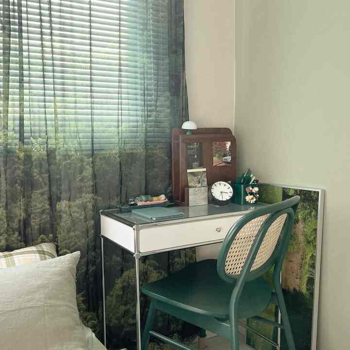 Natural-tone home office space featuring a green rattan chair, white desk, wooden vanity mirror, and clock creating a cozy work area