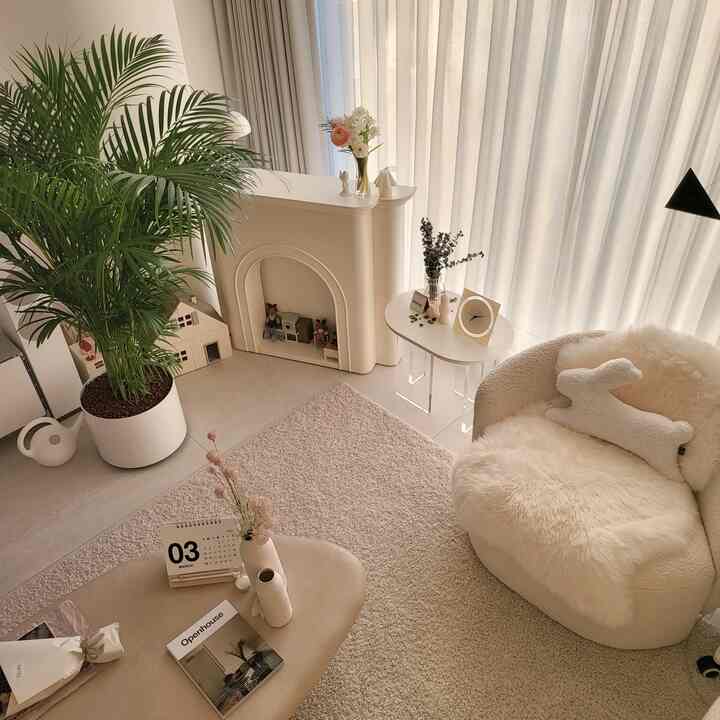 Bright ivory and beige toned living room with a soft fabric armchair, rug, and a large Areca Palm plant creating a cozy atmosphere