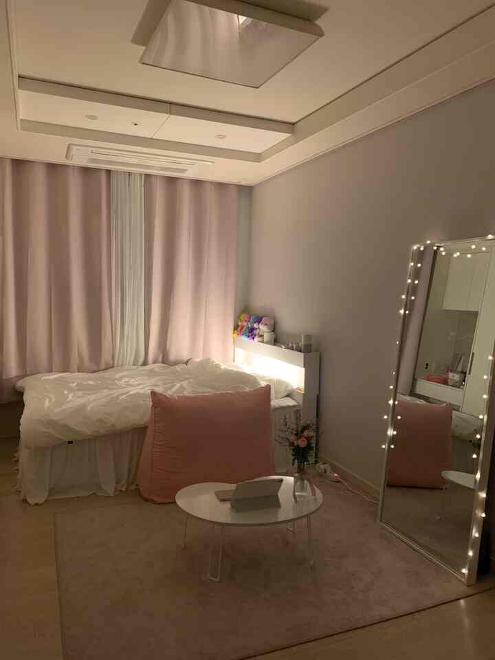 ピンクと白を基調とした寝室、ベッドとビーズクッション、カーテン、照明が配置された落ち着いた雰囲気のあるインテリア