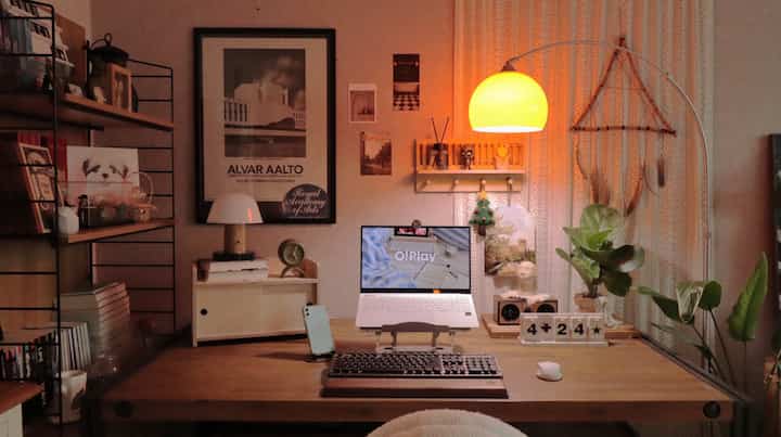 Cozy home office space with warm yellow lighting and natural wood tones, featuring a laptop on desk and framed wall decor