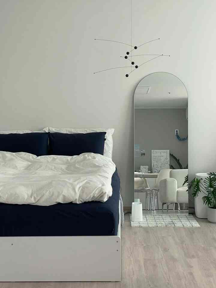 ホワイトとネイビーのトーンの寝室、ベッドと大型のアーチ型全身鏡が配置されたモダンで清潔感のあるインテリア