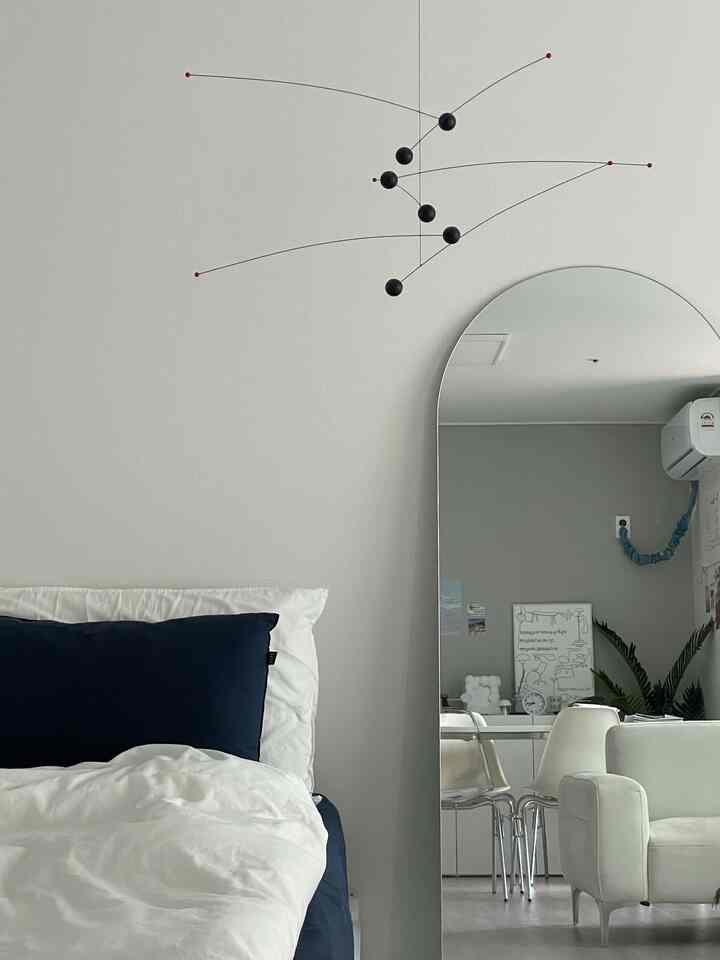 白とネイビーのトーンの寝室、モビールとアーチ型の全身鏡が配置されたモダンなインテリア