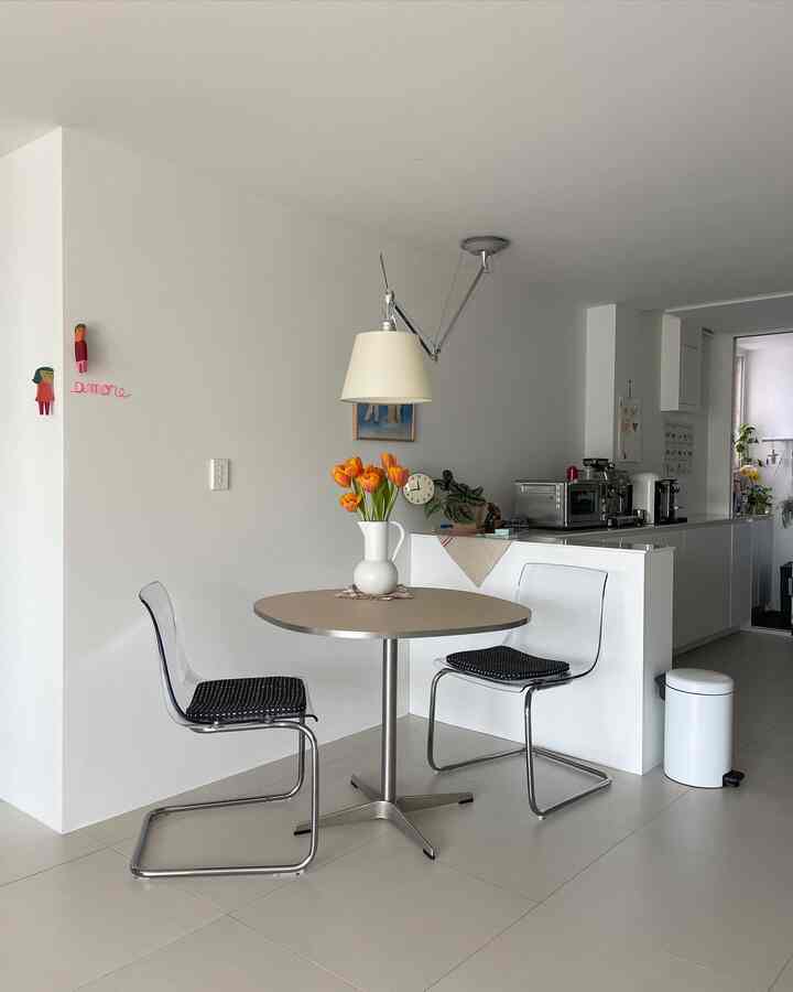 Modern and clean apartment kitchen space in white and beige tones featuring transparent chairs and a round dining table