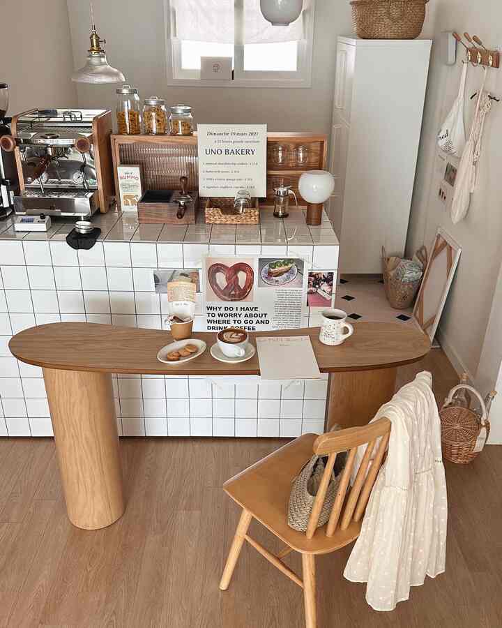 温かみのあるウッドトーンとベージュの調和がとれた落ち着いたキッチンダイニング空間、木製テーブルと椅子、コーヒーマシンと額装が配置されたシンプルなカフェ風インテリア