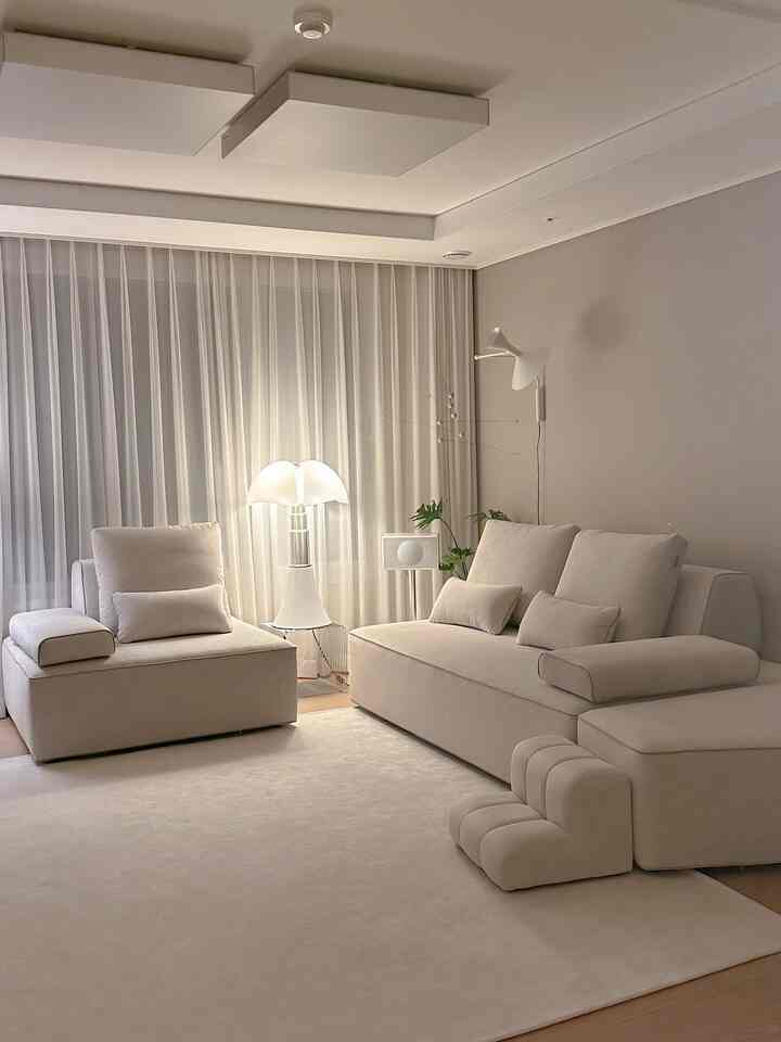 Warm white-toned living room featuring large sectional sofa, armchair, rug, and pet steps in a natural modern interior