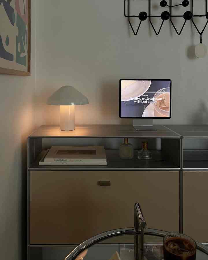 Calm beige and white toned home office space featuring a mushroom table lamp and tablet on a minimal storage cabinet