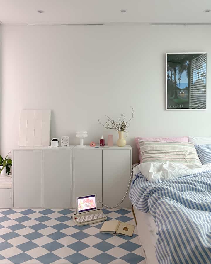 A bedroom with white and pastel blue tones featuring a checkered rug and pastel bedding that creates a cozy atmosphere