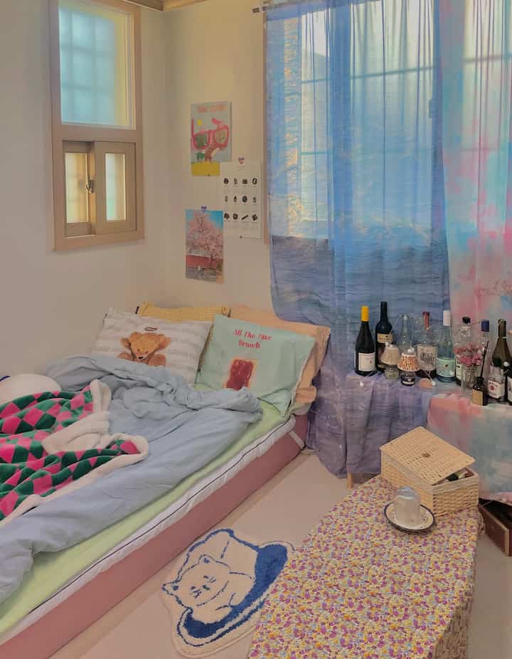 パステルブルーのトーンが特徴のワンルーム寝室、ベッドと青いシフォンカーテンが温かみのある雰囲気のインテリア