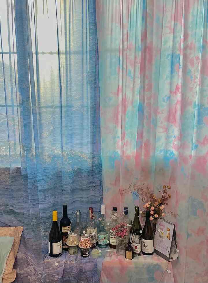 パステルとブルーの色調のカーテンとボトルが並ぶホームバーが配置された雰囲気のある空間
