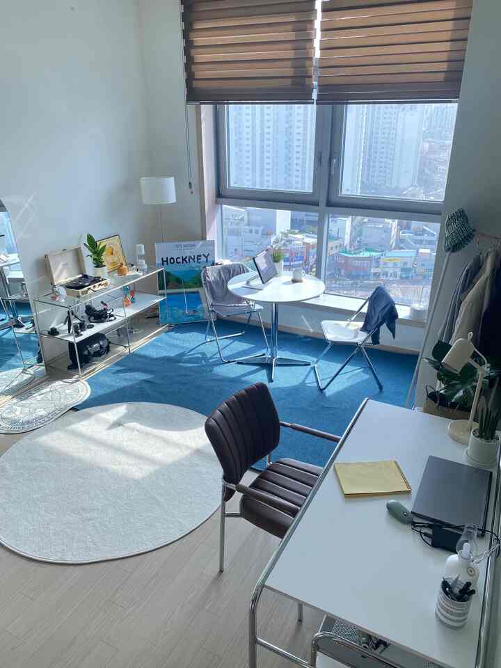 Mid-Century Modern home office in white and blue tones featuring large windows, a white desk with armchair, and a small round table with chairs