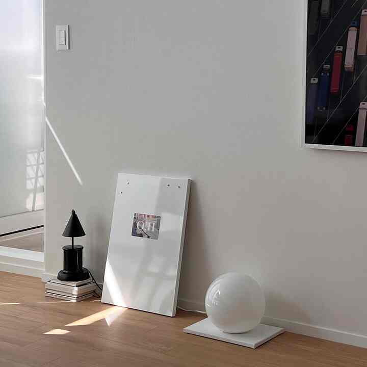Bright modern living room with white walls and wood tone flooring, featuring two minimalist lamps and a framed object on the floor