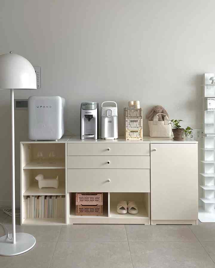 明るい白を基調としたリビング、中央にチェストと様々なベビー用品が整理されたモジュラー収納家具が配された清潔感のあるインテリア