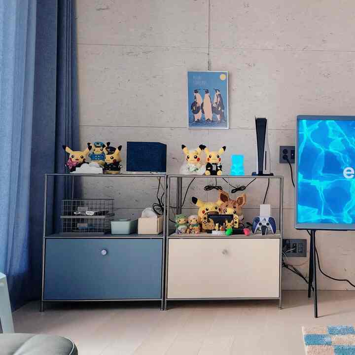 Sky blue and white toned kids' room featuring storage cabinets with Pikachu plushies and gaming devices in a cozy space