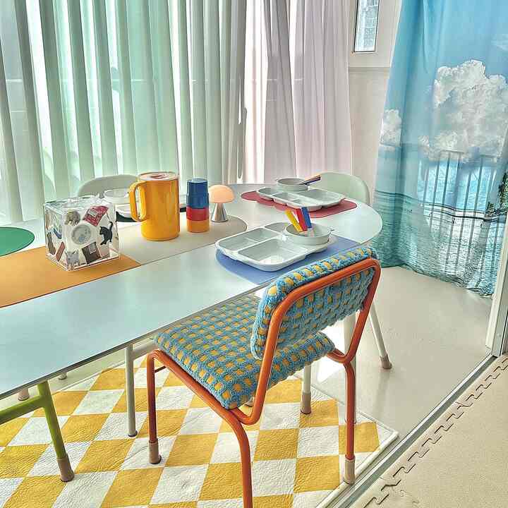 Dining room with white and pastel tone curtains, featuring colorful placemats and chairs creating a bright and lively atmosphere