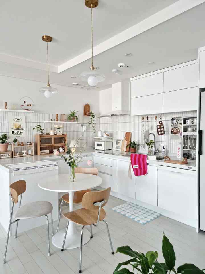 白を基調としたキッチン、中心に丸いダイニングテーブルと木製の椅子が配置された明るく清潔感のあるインテリア