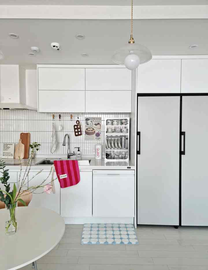 白を基調としたキッチン空間、食器洗い機と冷蔵庫、キッチンラック、フットレスト、エプロンが配置された清潔で機能的なインテリア