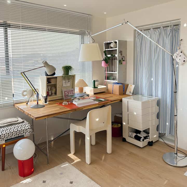 A bright workspace with white and wood tones, featuring a large wooden desk, chair, and multiple lamps, creating a clean home office atmosphere