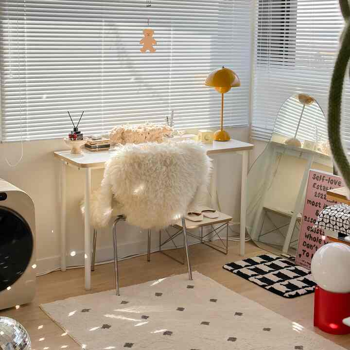 A compact studio home office in white and brown tones featuring a white desk and faux fur rug creating a cozy atmosphere