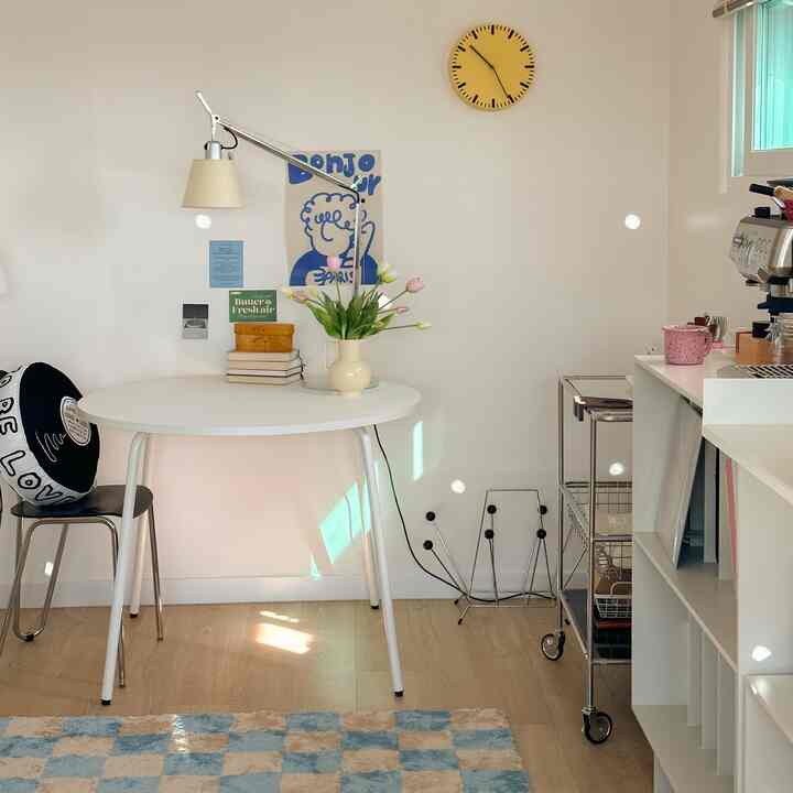 White-toned dining space featuring a round dining table, home cafe coffee machine, and yellow clock accent in a clean interior