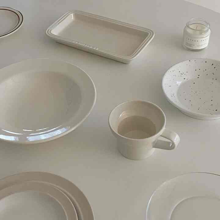 Ivory and white toned dining table featuring assorted bowls, cups, and a candle creating a neat home cafe atmosphere