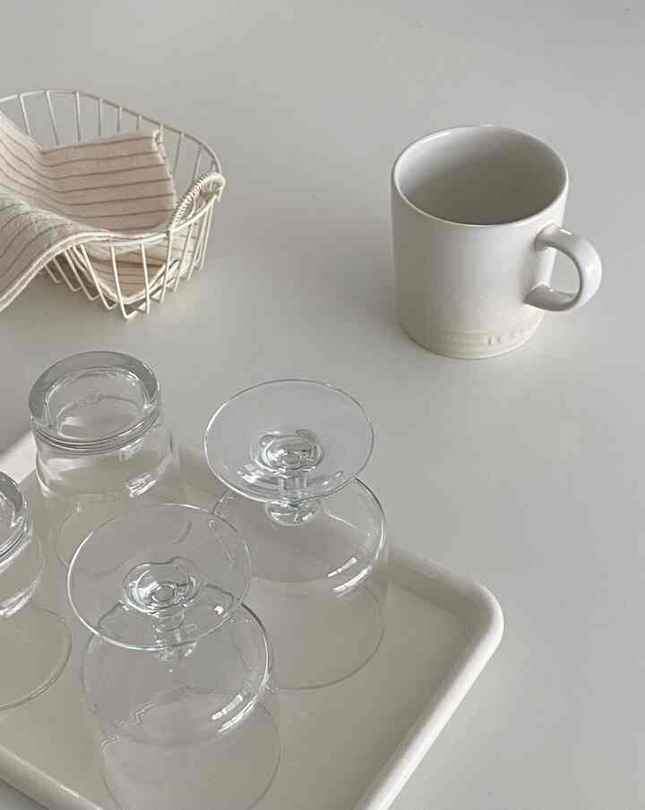 Monotone kitchen table featuring transparent glassware, a white mug, tray, and kitchen towel, creating a clean and minimal atmosphere