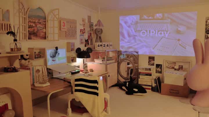 ピンクと木目調の調和が取れたロフトのワンルーム、机とプロジェクタースクリーンが配置された居心地の良いホームシネマ兼作業スペース