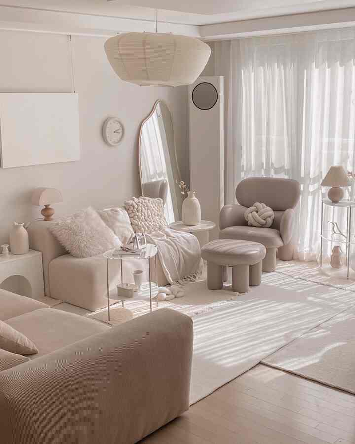 Bright white and beige toned living room featuring minimalist sofas, armchair, rug, and a tall mirror in a natural modern interior