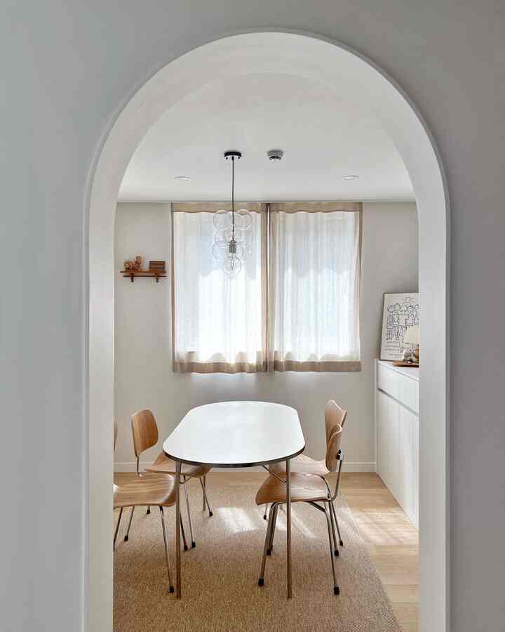 Natural dining room in white and wood tones, featuring a simple dining table and wood chairs framed by an archway with a cozy atmosphere