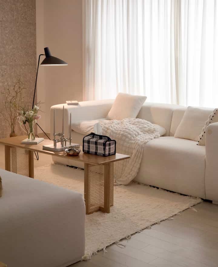 Bright white and beige toned living room featuring natural wood bench, sofa, and floor lamp creating cozy ambiance