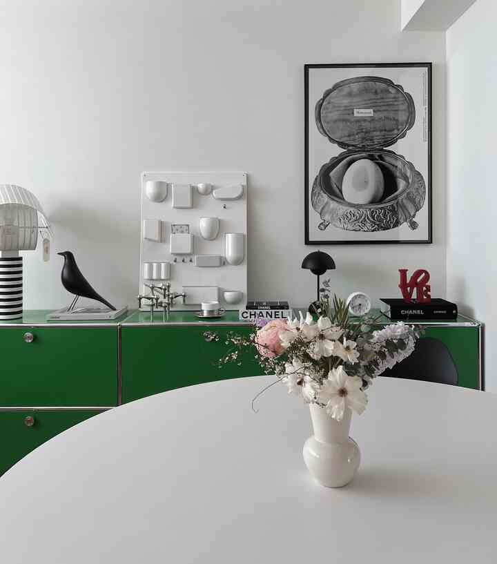 White and green toned living room featuring green storage cabinets and a white table with central vase, creating a clean atmosphere