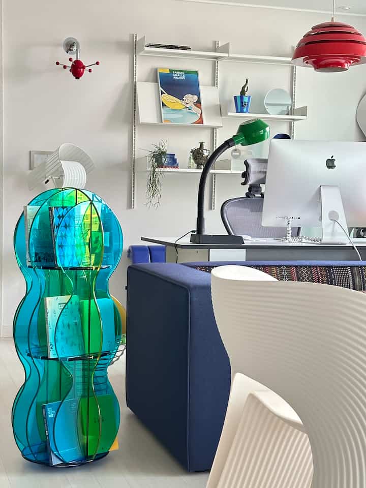 明るいナチュラルトーンの壁と床、青いソファと緑のデスクランプが配置されたモダンな書斎空間