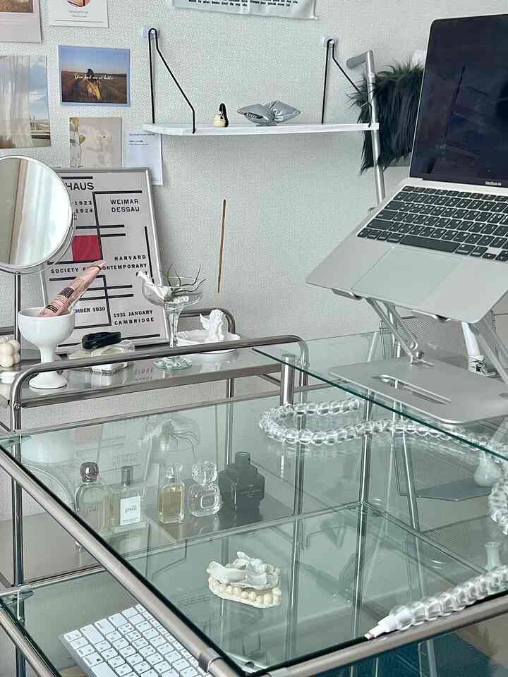 A white and metal-toned Mid-Century Modern home office with glass desk, shelves, and minimalist decor creating a clean natural atmosphere