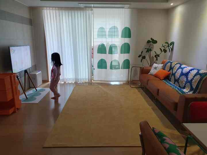 黄色のカーペットとブラウンのソファが配置されたシンプルでモダンな4人家族のリビング、子供がテレビを見ている