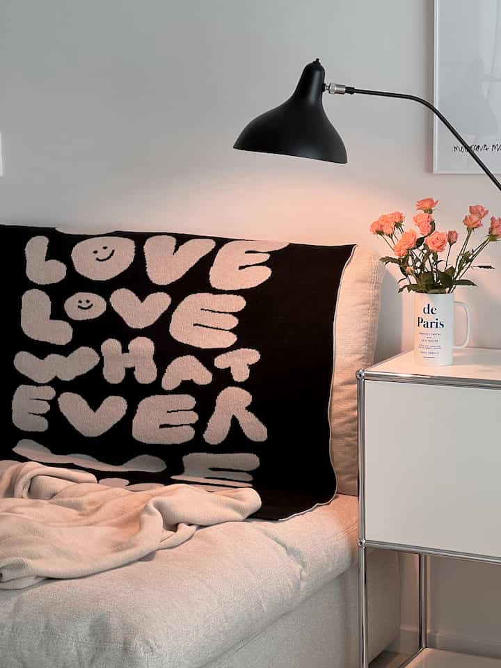 白とベージュの落ち着いたリビング、ベージュのソファと黒のテーブルランプ、ピンクのバラの花瓶が置かれたシンプルで清潔感のあるインテリア